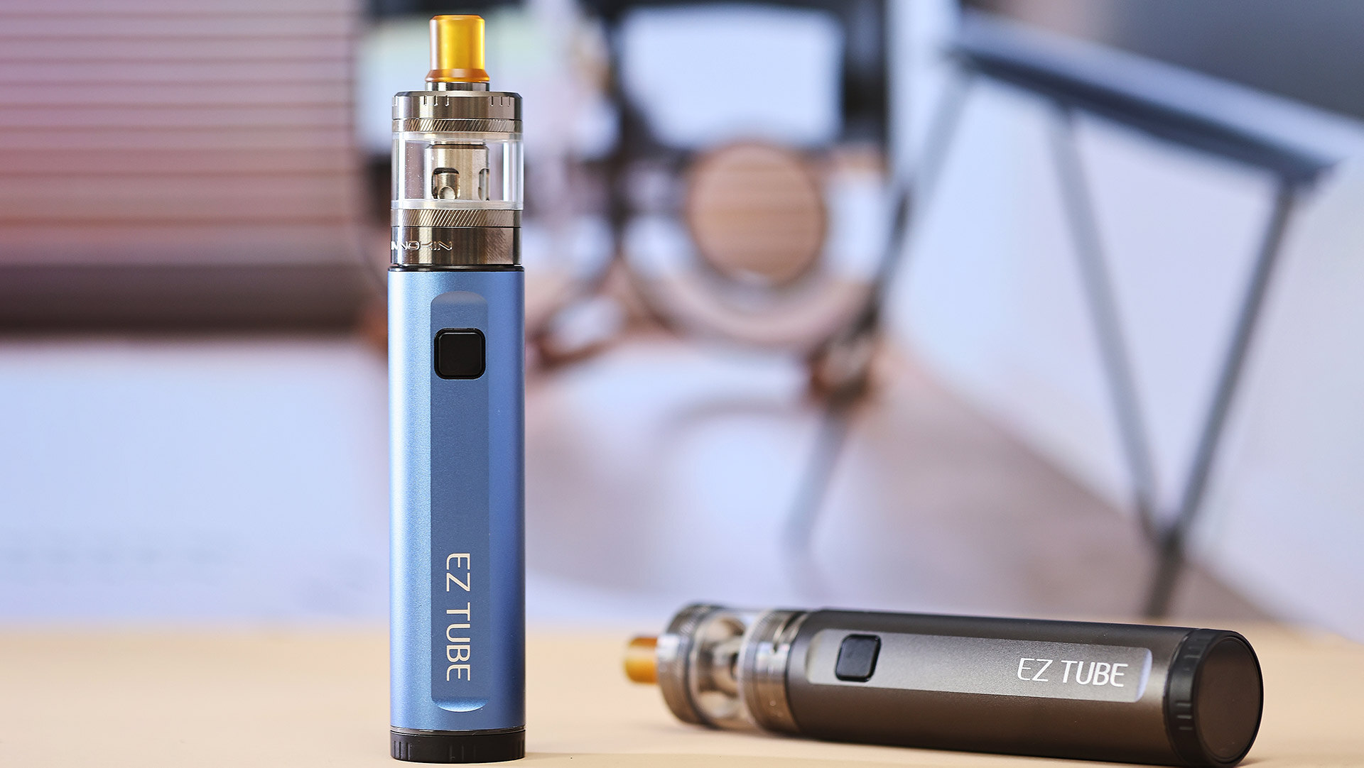 A close-up of two EZ TUBE vape pens on a table, one standing upright in a blue finish and the other lying horizontally in a darker shade, illustrating common troubleshooting issues when a vape pen isn’t working after charge, such as the device failing to detect the pod or cartridge.