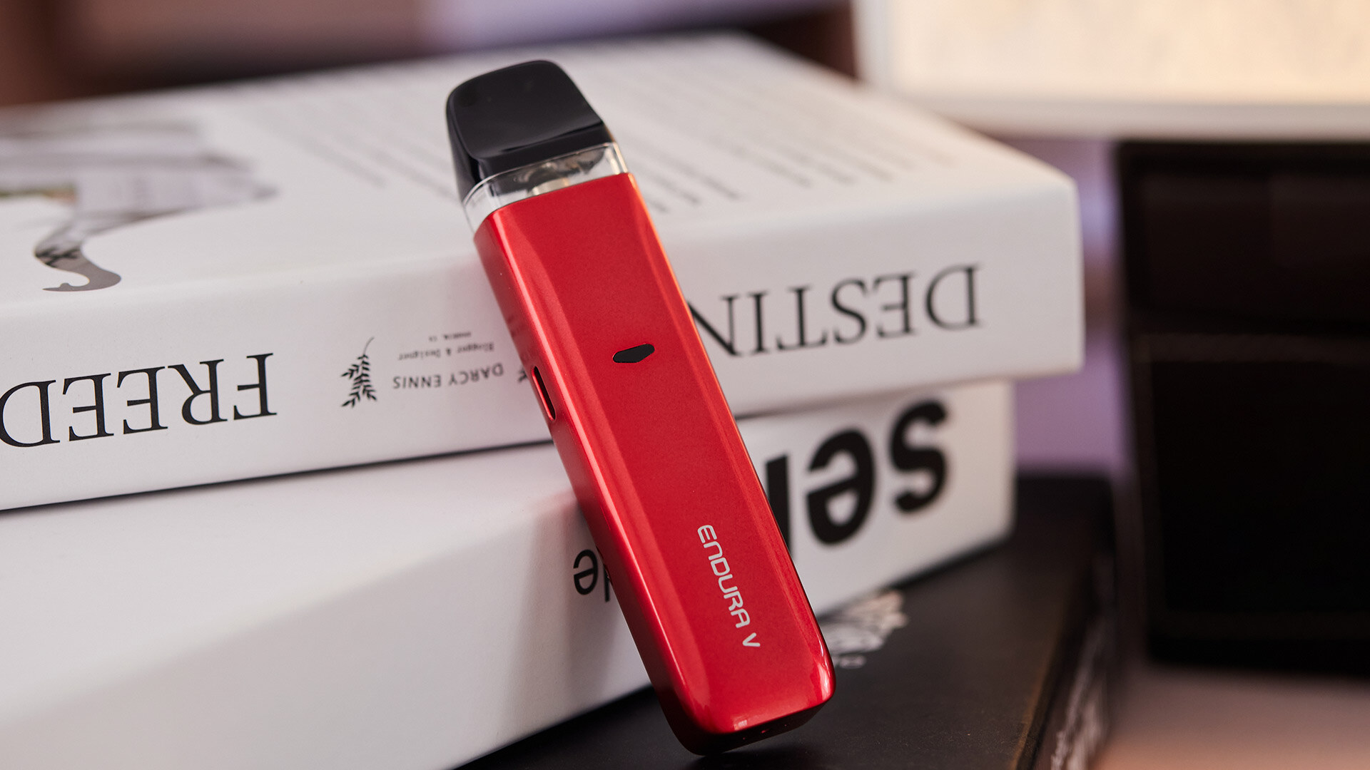 A red Endura V e-cigarette kit leaning against books.