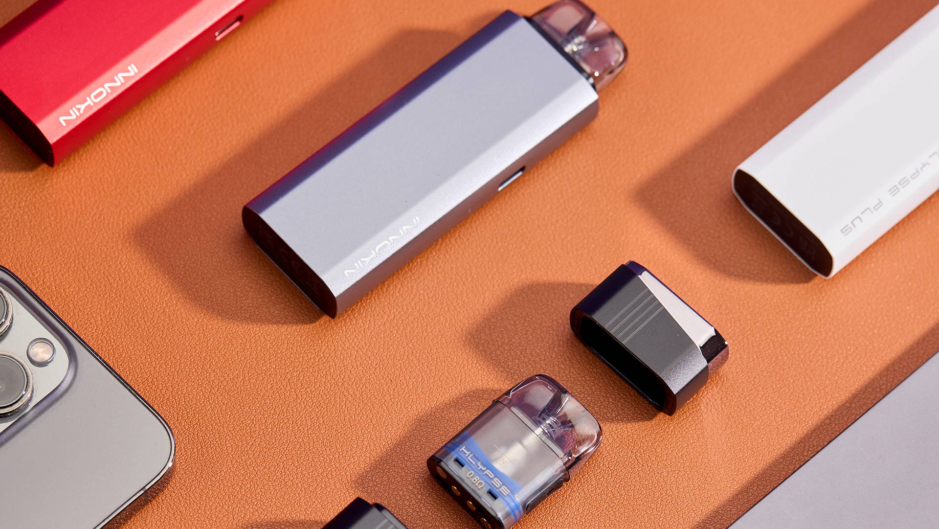 Innokin Klypse Plus pod system in various colors displayed on a textured orange surface.